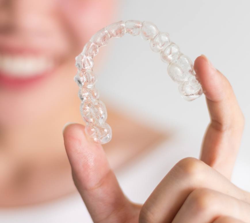 Smiling person holding a clear aligner