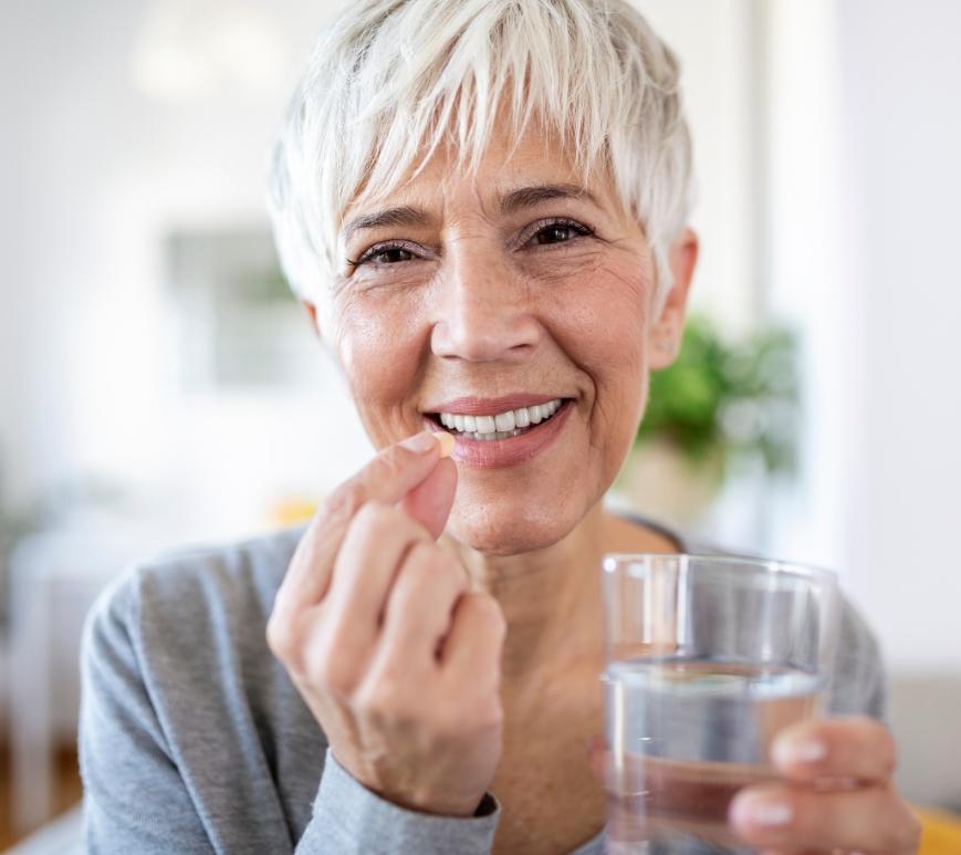 Senior woman holding a pill and a glass of water